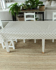 Bee pattern tablecloth in a dining room with a table and chairs on a textured rug, plants in the background