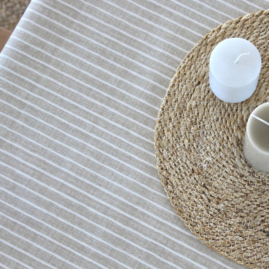 Close-up of a woven placemat with a candle on a striped tablecloth