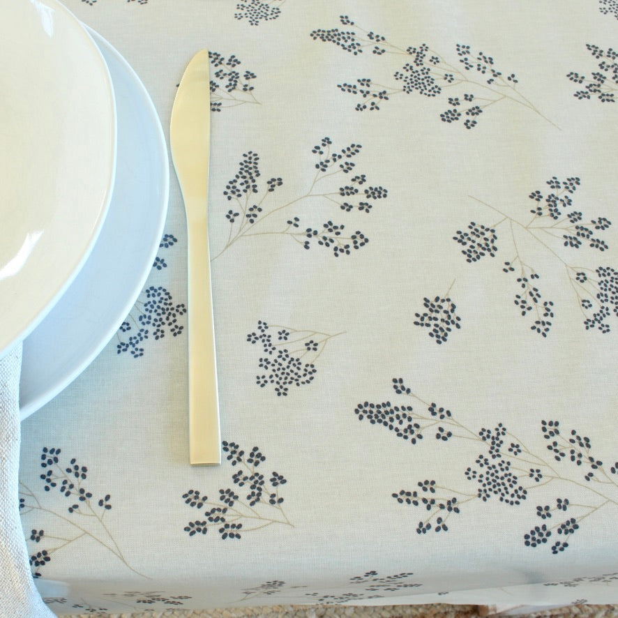 Table setting with a white plate, gold knife, and floral-patterned tablecloth.