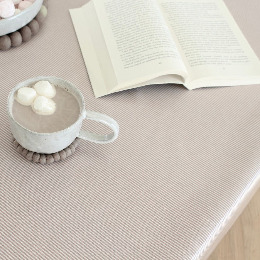 Cup of hot chocolate with marshmallows on a pink striped oilcloth next to an open book