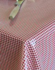 A close-up of a red and white gingham checkered tablecloth draped over a table, with a wooden-handled utensil resting on the surface.