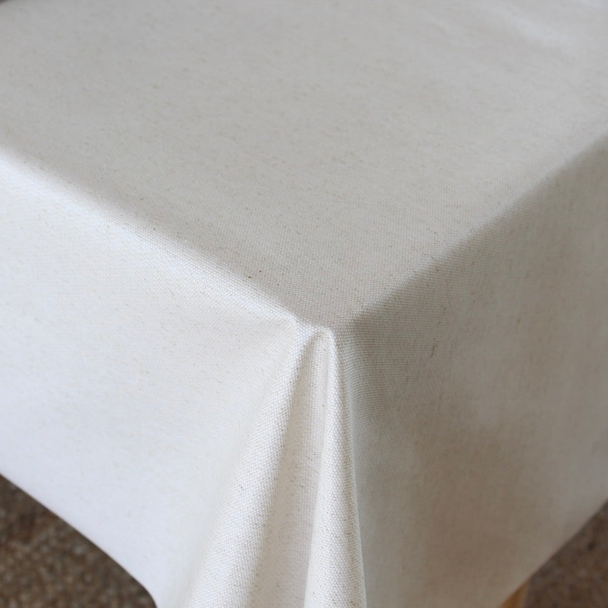 A close-up of a beige tablecloth draped over a table corner, showing its smooth texture and soft folds.