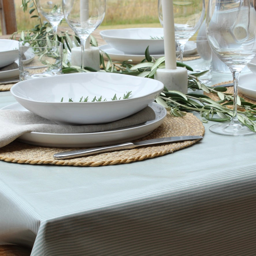 Elegant table setting with white plates, silverware, and greenery on a light blue tablecloth.