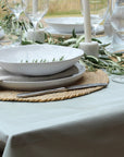Elegant table setting with white plates, silverware, and greenery on a light blue tablecloth.