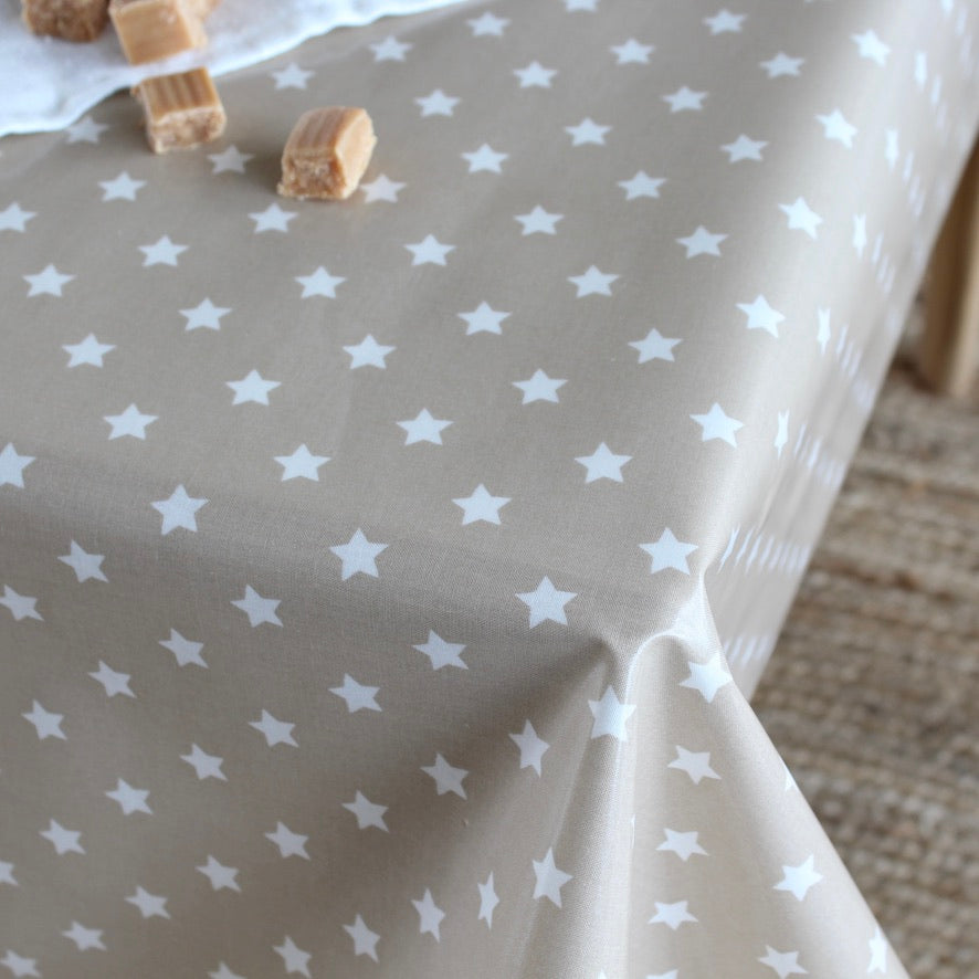 A close-up of a table covered with a beige tablecloth printed with a white star pattern, with a few small wrapped candies placed on the surface.