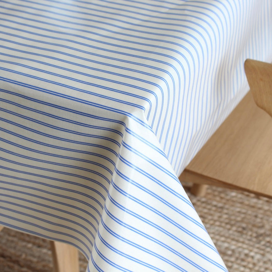 A close-up of a white tablecloth with thin blue horizontal stripes draped over a wooden table in a bright indoor setting.