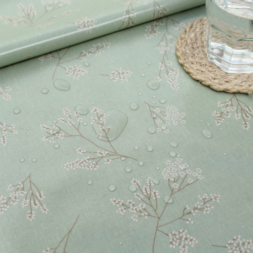 Light green oilcloth with floral pattern and a glass of water on a woven coaster.