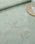 Light green oilcloth with floral pattern and a glass of water on a woven coaster.