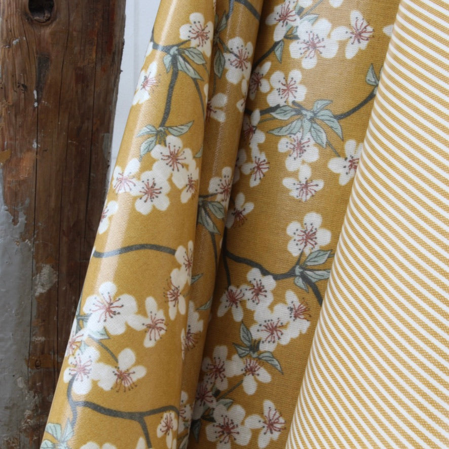Mustard yellow oilcloth with floral pattern next to a striped oilcloth.