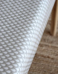 A close-up of a white tablecloth with a repeating gray teardrop pattern, draped over a table with a light wood leg visible on the right side.