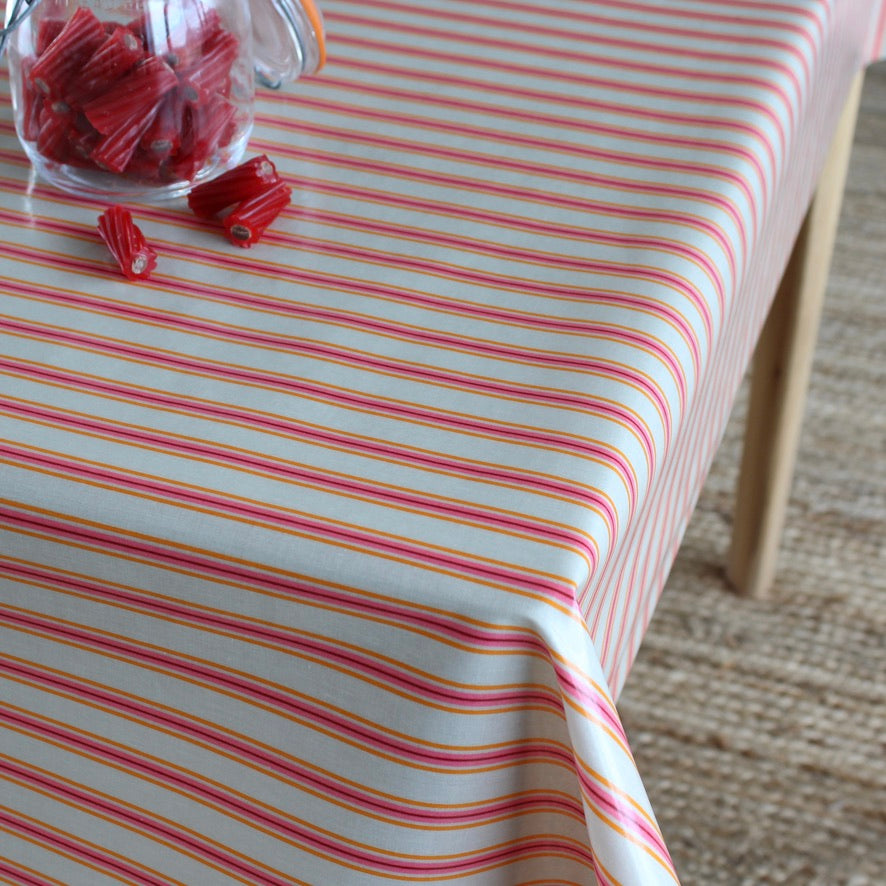 A close-up of a table covered with a tablecloth featuring thin red and pink horizontal stripes. A glass jar filled with red candy sits on the table, with a few pieces spilled.