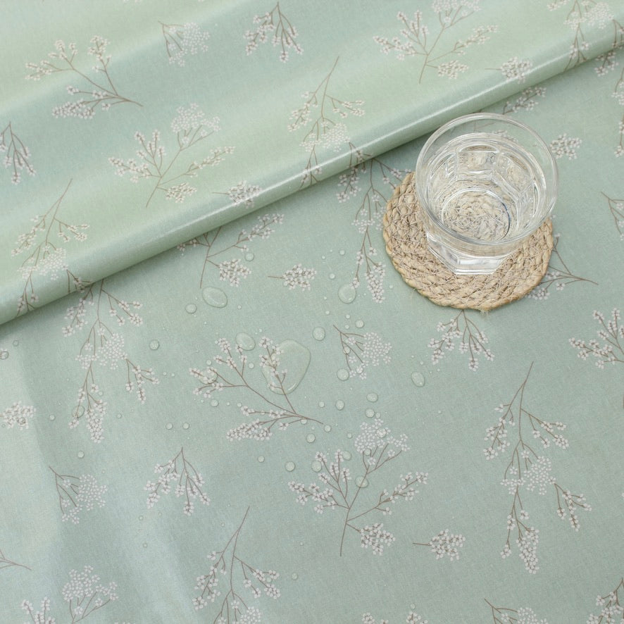Light green oilcloth with floral pattern and a glass of water on a woven coaster.