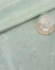 Light green oilcloth with floral pattern and a glass of water on a woven coaster.