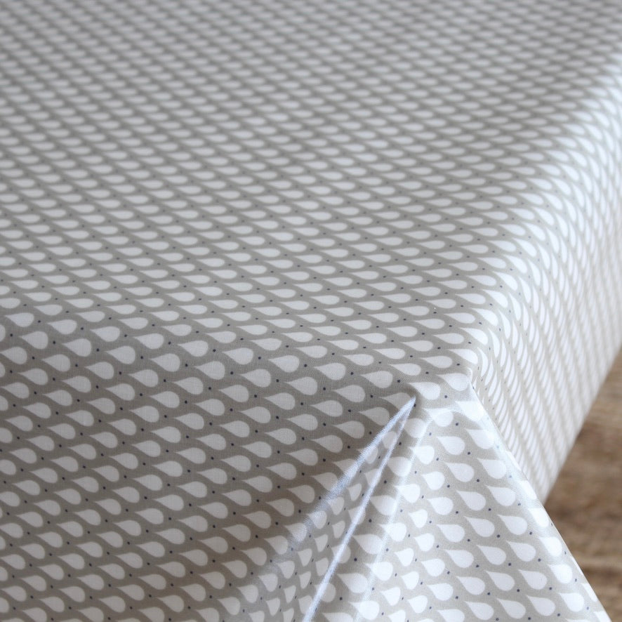 A close-up of a white tablecloth with a repeating gray teardrop pattern, draped over a table with a corner folded down to show the fabric's drape.