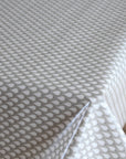 A close-up of a white tablecloth with a repeating gray teardrop pattern, draped over a table with a corner folded down to show the fabric's drape.