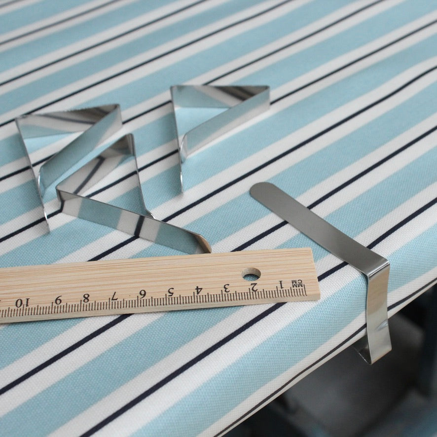 Metal tablecloth clips with a wooden ruler on a striped oilcloth