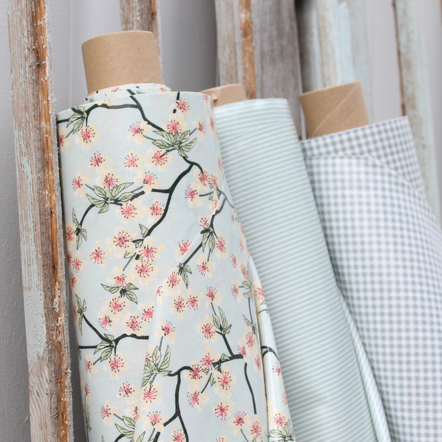 Rolls of oilcloth with floral and checkered patterns on a wooden stand.