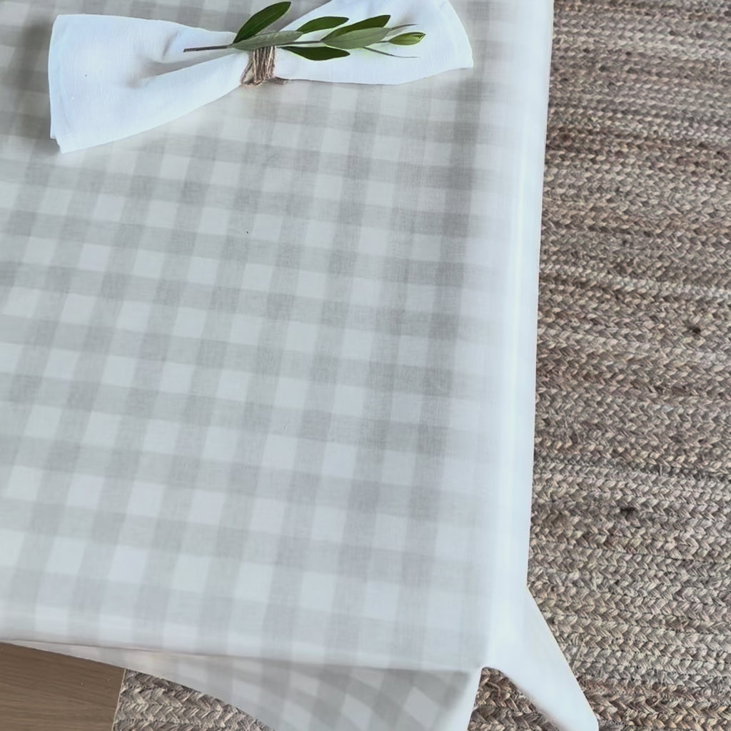 Beige gingham check oilcloth with a white linen napkin and an olive leaf sprig