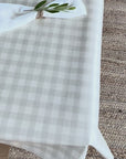 Beige gingham check oilcloth with a white linen napkin and an olive leaf sprig