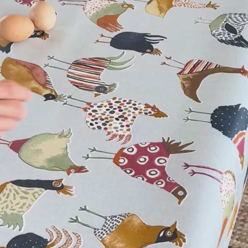 someone breaking an egg onto a chicken design oilcloth and wiping it up