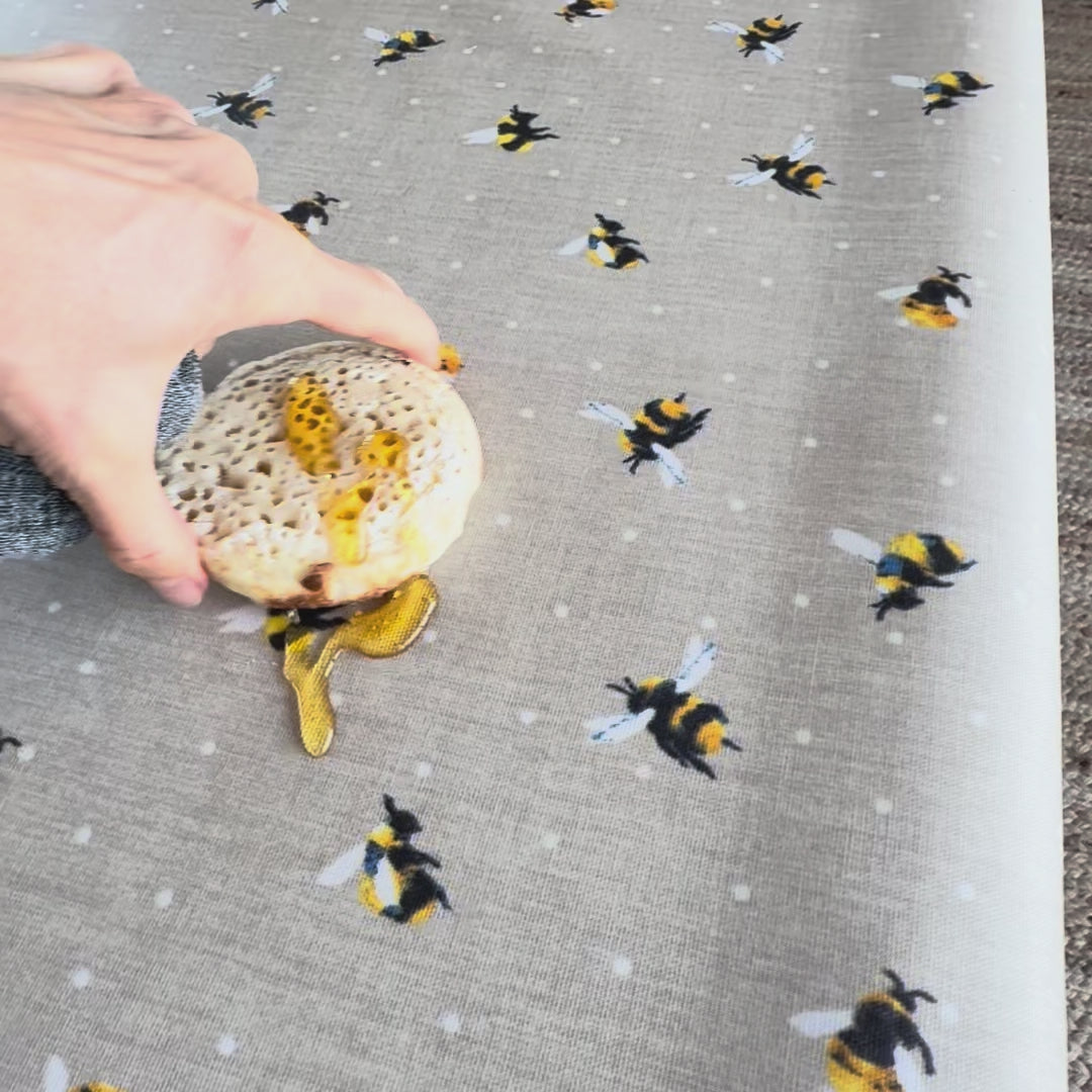 Bee design on a beige oilcloth with a crumpet and honey spilt onto the tablecloth.  The honey is then wiped off easily.