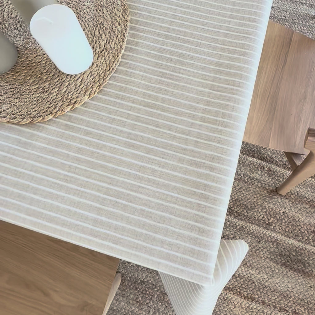 Beige and white stripe oilcloth on a wooden table with a jute table mat and candles