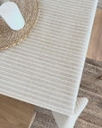Beige and white stripe oilcloth on a wooden table with a jute table mat and candles