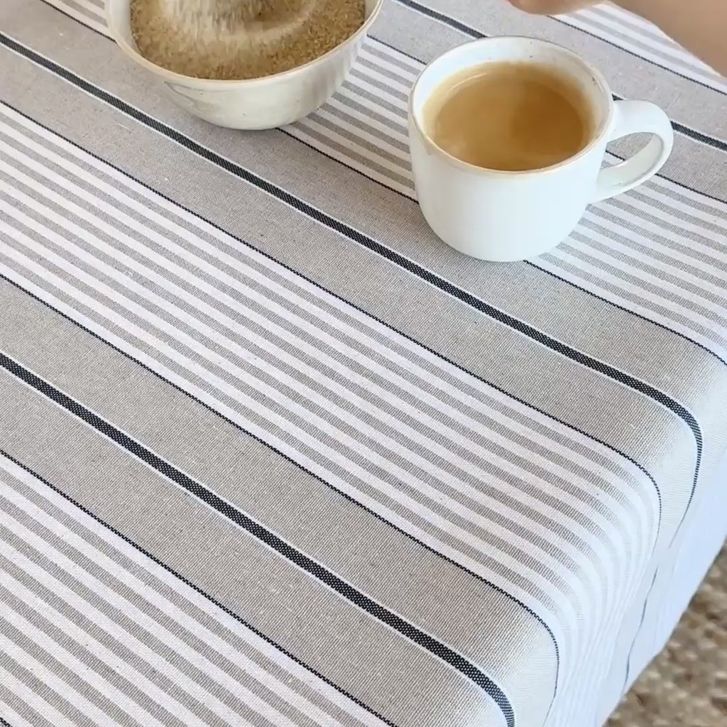 Coffee cup being stirred then spilt onto stripe blue and beige and white striped tablecloth then wiped clean with a paper towel.