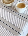 Coffee cup being stirred then spilt onto stripe blue and beige and white striped tablecloth then wiped clean with a paper towel.