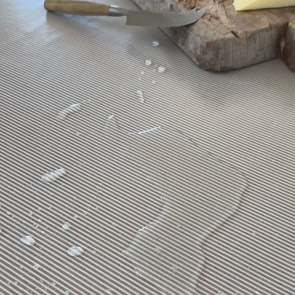 grey striped oilcloth with water spilt on top which is then wiped off with a paper towel
