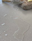 grey striped oilcloth with water spilt on top which is then wiped off with a paper towel