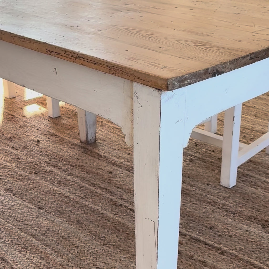 White tablecloth with blue flower pattern being put on a rustic wooden table.