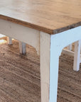 White tablecloth with blue flower pattern being put on a rustic wooden table.