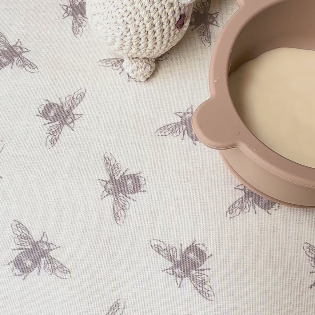 Baby food being dropped on a bee patterned beige tablecloth then wiped clean easily