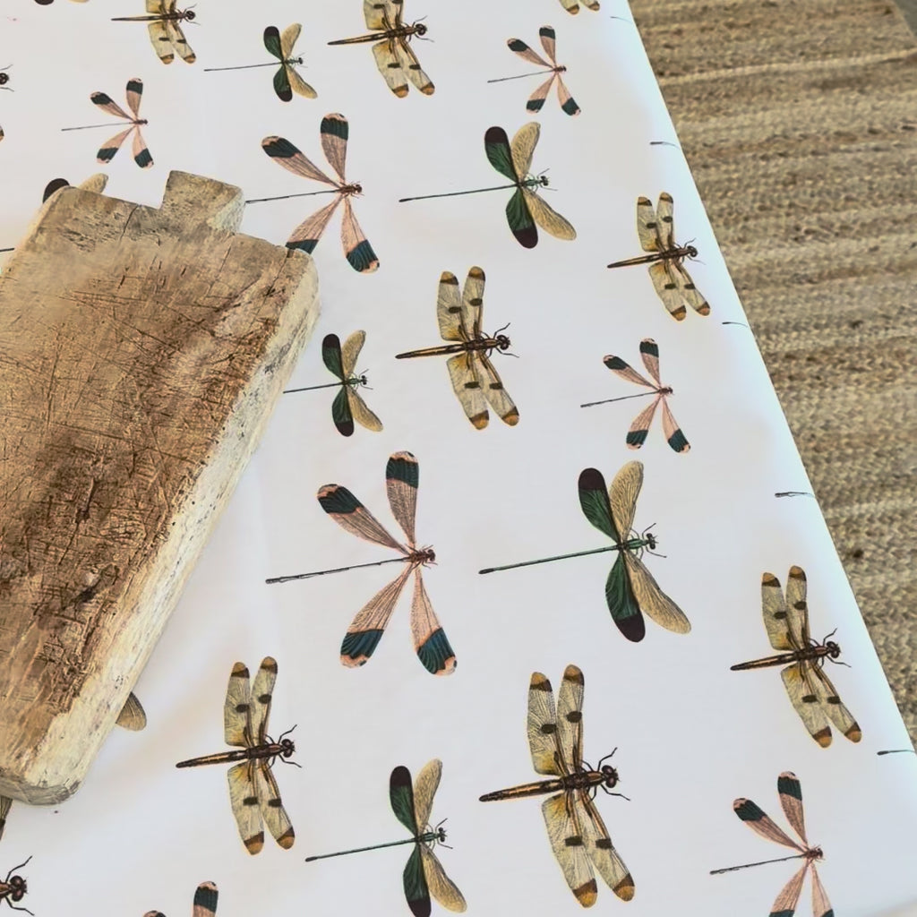 Dragonfly patterned oilcloth with a wooden board on a table.