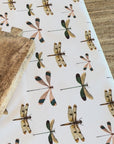 Dragonfly patterned oilcloth with a wooden board on a table.