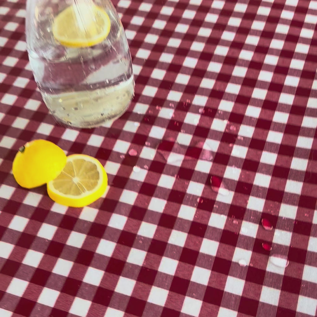 gingham red check tablecloth with water droplets sitting on top and a glass carafe with slices of lemon